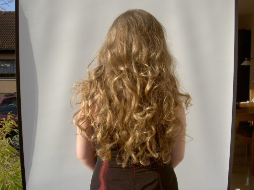 Hüftlanger Haarschnitt, naturgelockte Haare einer Person von hinten.